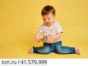 Toddler baby plays with a musical rattle bells on a stick, studio yellow background. Happy child musician playing percussion musical instrument, copy space. Kid aged one year and four months. Стоковое фото, фотограф Андрей Журавлев / Фотобанк Лори