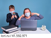 Junior boy in a school uniform prevents his mother from working remotely on a laptop. Problems when working from home during the coronavirus epidemic. Стоковое фото, фотограф Андрей Журавлев / Фотобанк Лори