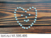 Beautiful heart formed by a handful of medicinal blue pills. Pills placed in the shape of a loving heart. Warfarin, anticoagulant, blood thinner. The topic of drug treatment to live. Wooden background. Стоковое фото, фотограф YuryKara / Фотобанк Лори