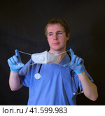 Doctor with a scar from respirator on his face n95 ffp2 in his hands on a dark background. Стоковое фото, фотограф Андрей Журавлев / Фотобанк Лори