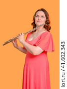 Portrait of a woman musician with a flute on a studio yellow background. Flutist with a large concert transverse flute in her hands. Стоковое фото, фотограф Андрей Журавлев / Фотобанк Лори