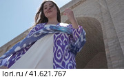 A young woman with long hair in an oriental robe and skullcap stands in the wind near an ancient mosque. Стоковое видео, видеограф Aleksey Kidisyuk / Фотобанк Лори