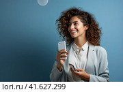 Молодая красивая девушка с телефоном в руке смотрит в сторону и улыбается. Место для надписи. Сгенерировано ИИ. Стоковое AI-изображение, AI-художник Ярославский Максим / Фотобанк Лори