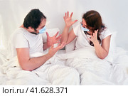 A man and a woman scream at each other while lying in a white bed. The concept of quarantine isolation problems due to the coronavirus epidemic. Стоковое фото, фотограф Андрей Журавлев / Фотобанк Лори