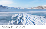 Video of winter landscape of frozen Baikal Lake in February cold sunny day. Сoastal mountains are covered with snow. Snow crusts in form of frozen waves on blue ice surface. Natural background. Стоковое видео, видеограф Виктория Катьянова / Фотобанк Лори