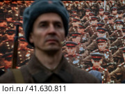 Мучжина в форме солдата и с оружием Великой Отечественной войны а фоне документальной кинохроники Парада Победы по Красной площади 1945 года в центре города Москвы, Россия (2023 год). Редакционное фото, фотограф Николай Винокуров / Фотобанк Лори