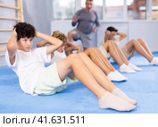 Underage boy practicing press in lying position with other attendees and trainer. Стоковое фото, фотограф Яков Филимонов / Фотобанк Лори