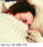 A woman with a coronavirus is covered with a blanket and squints while lying on the bed. Стоковое фото, фотограф Андрей Журавлев / Фотобанк Лори