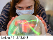 A gypsy woman wonders about the future of the coronavirus in 2021 on the ball of fate. Witch in a face mask over a crystal ball predicts the future of the flu virus in the new year. Стоковое фото, фотограф Андрей Журавлев / Фотобанк Лори