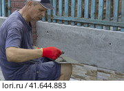 A male construction worker applies glue to the facing tile to lay it on the enclosing wall of the building from the outside. Стоковое фото, фотограф Светлана Зотова / Фотобанк Лори