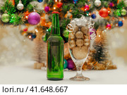 shiny christmas balls in a beer glass next to a green bottle and a decorated new year tree. Стоковое фото, фотограф Артем Курутин / Фотобанк Лори