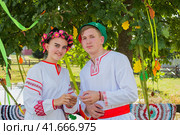 Клязьминский городок (Стародуб), Владимирская область, Россия. Август 2023 года. Юноша и девушка в ярких народных костюмах стоят под сенью зеленого дуба и смотрят в объектив.. Редакционное фото, фотограф Сергей Никифоров-Гордеев / Фотобанк Лори