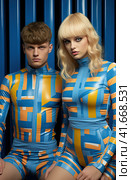 A young smiling cheerful couple, two friends, a family man and a woman in unusual blue designer clothes, stand next to each other, directing their gaze at the camera. Generated by AI. Стоковое AI-изображение, AI-художник Ярославский Максим / Фотобанк Лори