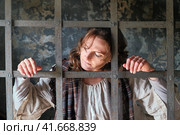 A young woman imprisoned sadly looks out from behind bars in a medieval prison. Portrait of a criminal in vintage clothes at a Halloween party. Стоковое фото, фотограф Андрей Журавлев / Фотобанк Лори