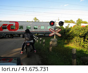 Pavelets, Russia - July 29, 2019. Motorcyclist standing at the railroad crossing. Summer sunset view. Мотоциклист на железнодорожном переезде ждет, пока проедет поезд. Редакционное фото, фотограф Александр Кузнецов / Фотобанк Лори