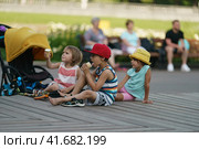 Moscow, Russia - June 22, 2021:  Group of children sitting on the wooden in the public park. They eat ice cream in waffle cups. Having fun stylish children. Happiness of childhood. Leisure concept. Редакционное фото, фотограф YuryKara / Фотобанк Лори