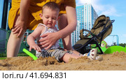 Little baby learns to play with sand in a children's sandbox under the control of a mother woman. Kid aged one year. Стоковое видео, видеограф Андрей Журавлев / Фотобанк Лори