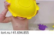 Baby drinks water from a ladle while sitting with toys in a white bathtub A happy child enjoys washing in the bathroom. Kid aged one year six months (18 months) Стоковое видео, видеограф Андрей Журавлев / Фотобанк Лори