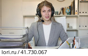 Young positive woman customer support phone operator in microphone headset working on laptop in the office. Стоковое видео, видеограф Яков Филимонов / Фотобанк Лори