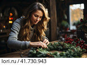 Young Cute smiling Woman designer preparing Christmas Evergreen Tree Wreath. Manufacturer of Christmas decor with their own hands. Christmas wreath for the holiday. The new year celebration. Closeup. Стоковое AI-изображение, AI-художник Ирина Михайличенко / Фотобанк Лори