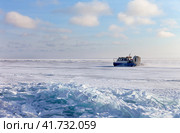 Tourists travel by Khivus airboat across frozen Baikal Lake from village of Listvyanka to village of Goloustnoye on cold sunny January day. Scenic winter landscape. Natural background. Winter travel. Стоковое фото, фотограф Виктория Катьянова / Фотобанк Лори