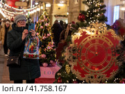 Женщина фотографирует дизайнерскую ель в ГУМе украшенный в преддверии новогодних праздников в городе Москве, Россия (2023 год). Редакционное фото, фотограф Николай Винокуров / Фотобанк Лори