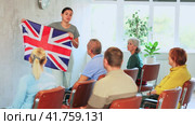 Emotional young female tutor showing national flag of United Kingdom while leading english language club for group of elderly people sitting in auditorium. Стоковое видео, видеограф Яков Филимонов / Фотобанк Лори