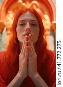 A beautiful girl in a red shirt and with red hair folded her hands prayerfully in front of her face. Стоковое AI-изображение, AI-художник Ярославский Максим / Фотобанк Лори