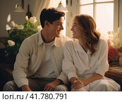 A young cute couple is sitting on a sofa in front of a window with white flowers and smiling at each other. Стоковое AI-изображение, AI-художник Ярославский Максим / Фотобанк Лори