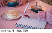Woman Writing Plan in a Notepad Sitting on a Pink Cafe Table with Coffee Cup and Dessert. Hand Close up. New Year Routine, Resolution. Goals, To Do List in the Notebook. Action, Checklist Idea Concept. Стоковое видео, видеограф Марина Демидюк / Фотобанк Лори
