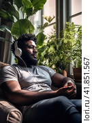Self absorbed dark skinned mid adult man in headphones sits in armchair. Window, green house plants. Стоковое AI-изображение, AI-художник Наталья Семкина / Фотобанк Лори