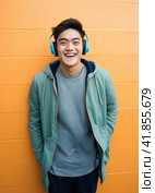 Joyful asian young man in blue headphones standing on orange wall background. Стоковое AI-изображение, AI-художник Наталья Семкина / Фотобанк Лори