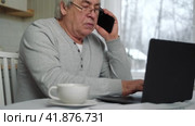 Serious senior man wearing glasses Talking mobile phone sitting at desk at home workplace with laptop. Retired male working chatting colleagues. Old worker talk on cellphone work on computer gadget. Стоковое видео, видеограф Марина Демидюк / Фотобанк Лори