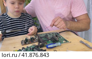 Father with his son spend time together. Close-up of a man teaching his boy at home to solder computer spare parts. Education moment during parenthood. Togetherness concept. Стоковое видео, видеограф Ирина Старикова / Фотобанк Лори