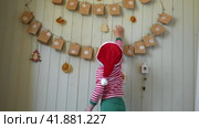 Boy in pajamas, Santa cap eating sweet candy on paper advent calendar with presents background. Little happy child with gift of handmade Christmas calendar on wall. Celebrating at home Xmas tradition. Стоковое видео, видеограф Марина Демидюк / Фотобанк Лори