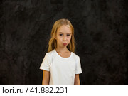 Portrait of frowning cover girl kid model 6 year old in white t-shirt expression emotion, angry looking at camera. Scowl child posing at black, studio shot. Kids emotional concept. Copy ad text space. Стоковое фото, фотограф Aleksandr Golubev / Фотобанк Лори