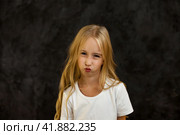 Portrait of scowl cover girl kid model in white t-shirt expression emotion, frowning looking at camera. Angry child 6 year old posing at black, studio shot. Kids emotional concept. Copy ad text space. Стоковое фото, фотограф Aleksandr Golubev / Фотобанк Лори