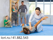 Woman is learning how to grab opponent's hand in prone position during self-defense class, in background girl and boy watch sparring. Стоковое фото, фотограф Яков Филимонов / Фотобанк Лори
