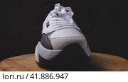 White women's sneaker with the outside and front side facing the camera standing on a wooden surface. Dark background. The camera flies around. Parallax effect. Krasnodar, Russia, April 19, 2022. Редакционное видео, видеограф Воловодов Владимир / Фотобанк Лори