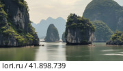 Beautiful view of the sea bay with karst limestone islets and cliffs on a cloudy day. Стоковое AI-изображение, AI-художник Евгений Харитонов / Фотобанк Лори