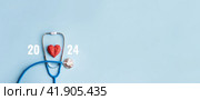 Stethoscope, red decorative heart and numbers 2024 on blue background. Medical New Year banner for clinic. Selective focus, copy space. Стоковое фото, фотограф Клара Мухаметзянова / Фотобанк Лори