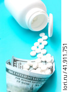 A white jar with pills lies on a blue background. Next to it is a bag made of a hundred dollar bill. Стоковое фото, фотограф Ярославский Максим / Фотобанк Лори