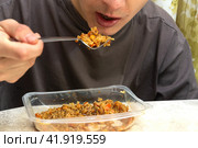 A man eats pilaf from disposable plastic dishes with a fork. Стоковое фото, фотограф Ярославский Максим / Фотобанк Лори