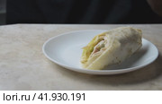 A young man takes a shawarma from a plate and eats it. A cinematic picture. Passage from left to right. Стоковое видео, видеограф Ярославский Максим / Фотобанк Лори