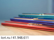 A stack of books in colorful covers lying on the surface of the table, low depth of field. The concept of "Back to school". School and office supplies on a wooden background. Several colorful diaries. Стоковое фото, фотограф Александр Кротков / Фотобанк Лори