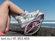 Close-up sportswoman legs in Kangoo Jumps boots on beach while resting during aerobic training session workout. Side view, low angle shot (2022 год). Редакционное фото, фотограф А. А. Пирагис / Фотобанк Лори