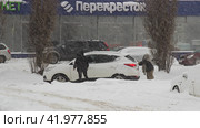 Зима. Метель. Женщина толкает буксующий автомобиль. Липецк. (2024 год). Редакционное фото, фотограф Евгений Будюкин / Фотобанк Лори