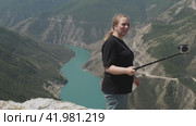 Девушка стоит на краю каньона с зеленой водой. Снимает себя на камеру и рассказывает о своих впечатлениях. Концепция путешествия с камерой. Стоковое видео, видеограф Воловодов Владимир / Фотобанк Лори