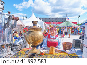 Traditional Irbit fair, Russia.Senior woman in festive folk clothes.Table with big old metal samovar (2023 год). Редакционное фото, фотограф Ирина Кононова / Фотобанк Лори
