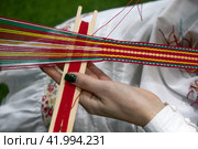 Крупным планом девушка ткет тесьму со славянским орнаментом (2024 год). Редакционное фото, фотограф Николай Винокуров / Фотобанк Лори